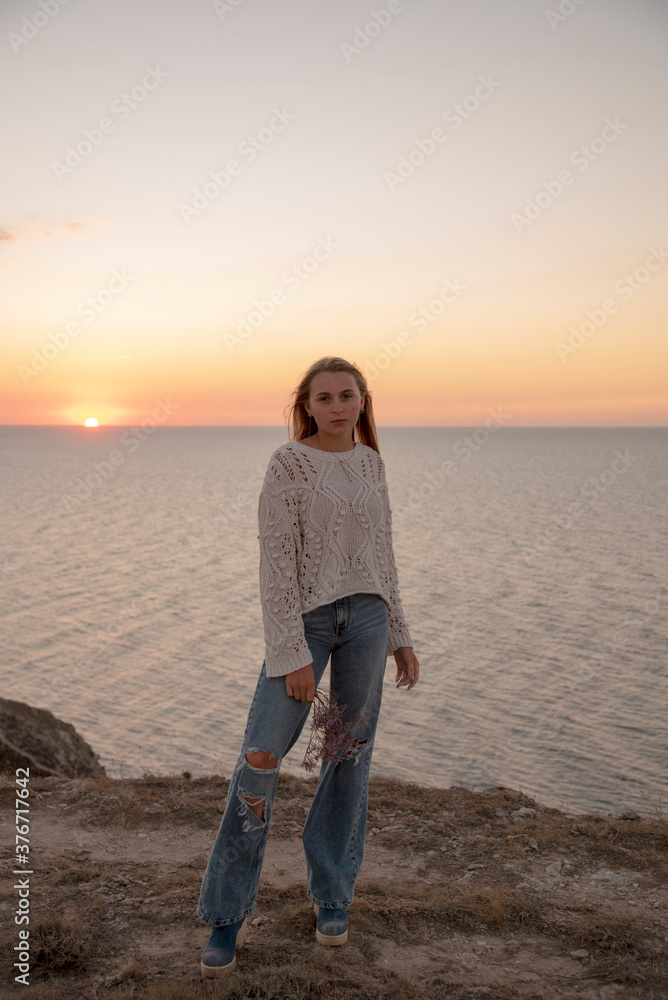 A blonde girl in leaky jeans poses against the background of the sunset .