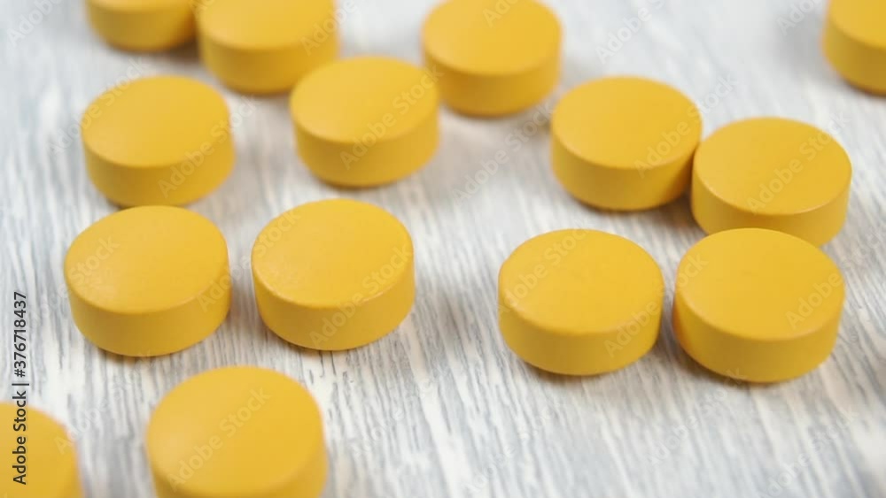 Yellow round medical pill falls into a pile of medicines on a wooden table close-up. Macro shot. Selective focus Yellow round medical pill falls into a pile of medicines on a wooden table close-up. Macro shot. Selective focus