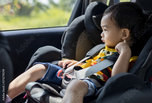 Adorable Asian kid boy (Toddler age 1-year-old) Protection Sitting in the Car Seat with Safety Belt Locked. photo