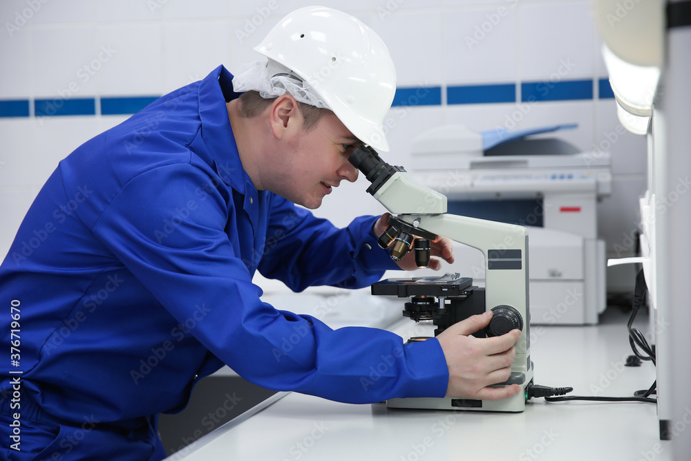 laboratory worker in blue clothes looking through a microscope