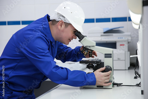 laboratory worker in blue clothes looking through a microscope