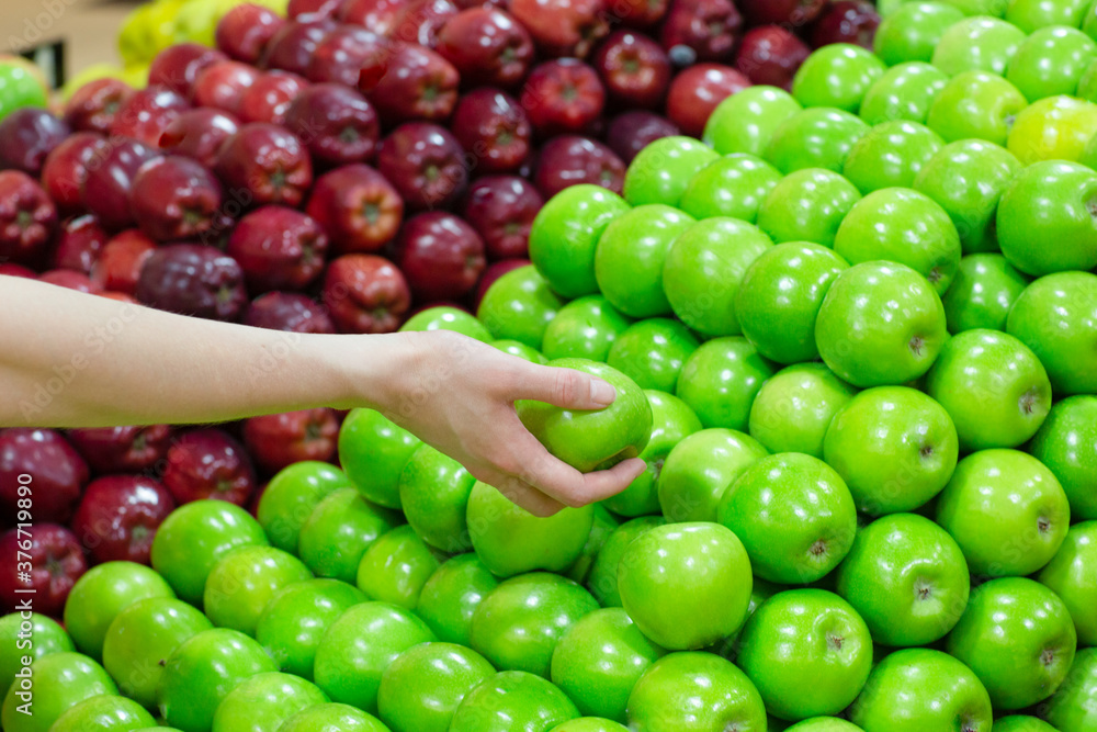 Closeup of a person's hand choosing a green apple from a pile at the grocery food market stall. Closeup of a person's hand choosing a green apple from a pile at the grocery food market stall.