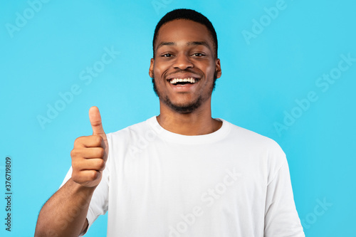 Cheerful African American Guy Gesturing Thumbs-Up Posing Over Blue Background