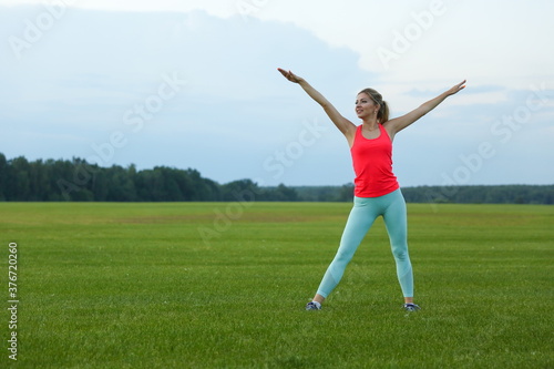 young woman doing yoga exercises on a large meadow of lawn grass © Петр Смагин
