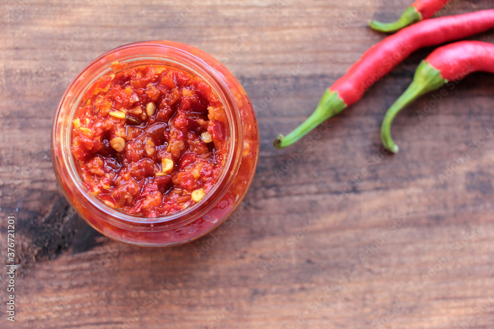 Fresh fed hot chili peppers and canned sauce in glass jar on wooden table background. Top view, copy space Fresh fed hot chili peppers and canned sauce in glass jar on wooden table background. Top view, copy space