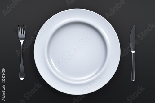 Empty ceramic plate with fork and knife on a dark table. View from above.