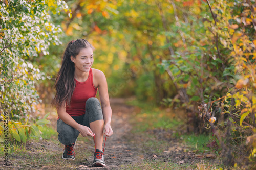 Autumn outdoor exercise lifestyle. Asian runner woman tying running shoes ready to run for fitness cardio workout in forest nature.