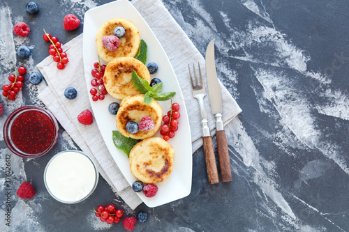 Tasty cheese pancakes with berries  bowls with jam and cream on grey background