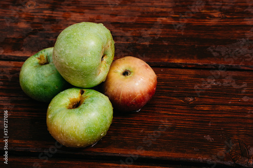 Fresh autumn Apple harvest on the kitchen countertop. Four fresh apples lie on a wooden table. A textured mahogany wood background and fruit lie on it.