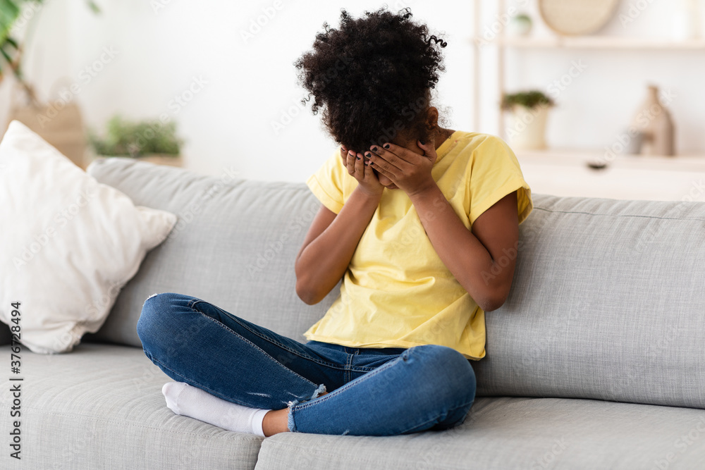 Fototapeta premium Depressed African Girl Crying Covering Face Feeling Sad Sitting Indoor