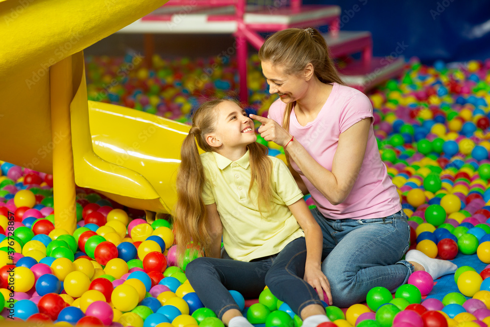 Obraz premium Loving mother and her child sitting in ball pit at indoor playground, copy space