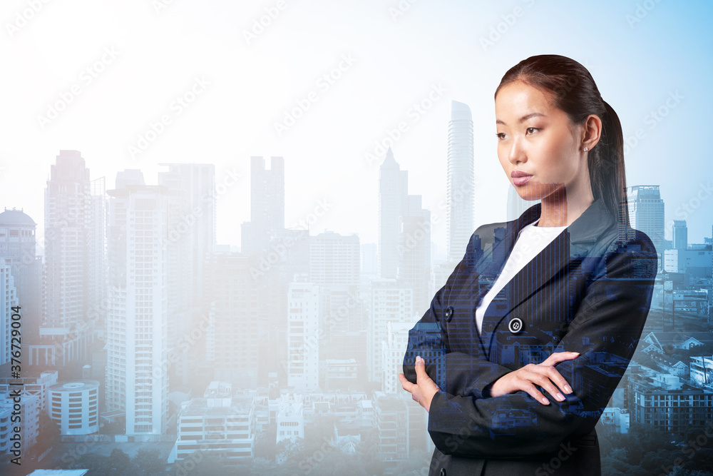 Prosperous Asian businesswoman in suit in crossed arms pose. Bangkok cityscape. The concept of woman in business. Financial downtown. Double exposure. Prosperous Asian businesswoman in suit in crossed arms pose. Bangkok cityscape. The concept of woman in business. Financial downtown. Double exposure.