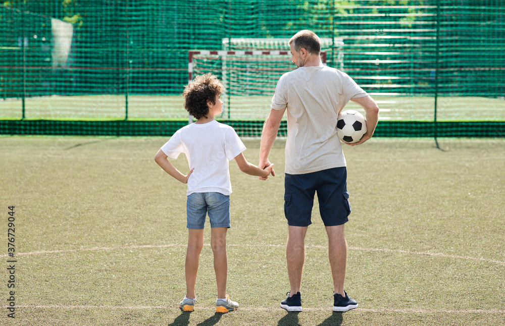 Man posing with little boy on football pitch back view