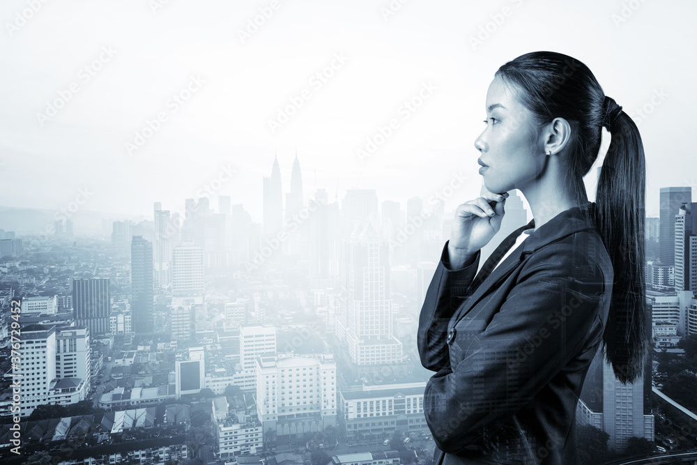 Attractive young Asian business woman in suit with hand on chin thinking how to succeed, new career opportunities, MBA. Kuala Lumpur on background. Double exposure. Attractive young Asian business woman in suit with hand on chin thinking how to succeed, new career opportunities, MBA. Kuala Lumpur on background. Double exposure.