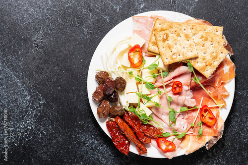 Assortment of tasty food on the plate. Italian antipasto on black stone table top view. copy space for your text.