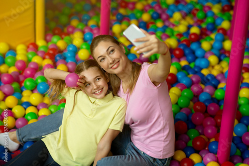 Mother and daughter taking selfie together in ball pond at kids play center