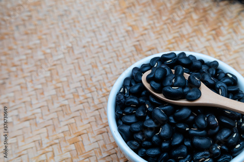 Black beans in a wooden spoon with a white ceramic bowl, placed on a wooden tray. photo