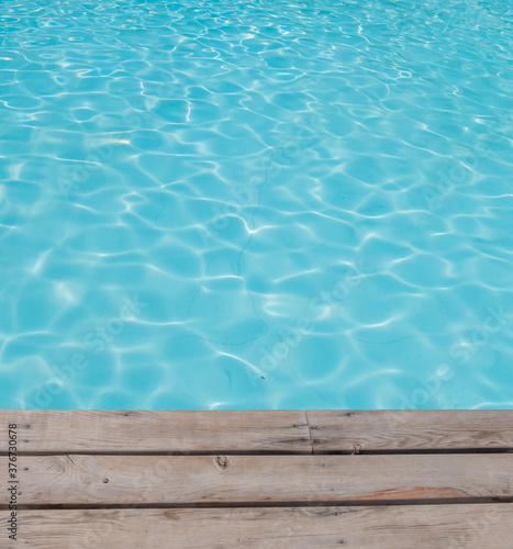 Blue tiles pool water ripple texture and wooden background.