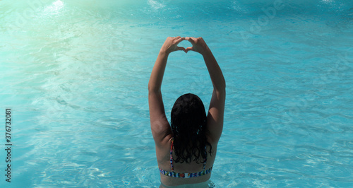 Young woman showing a heart symbol with hands at pool.