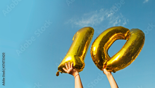 The child is holding balloons 1 and 0 against the sky. Place for your text. Birthday celebration concept.