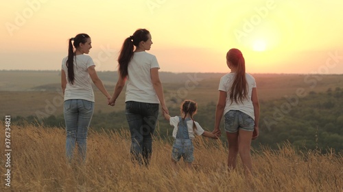 healthy family, mom and daughters are walking in field at sunset in mountains, children are holding mom's hands. happy children and parent walk in rays of the beautiful sun, travel. happy family