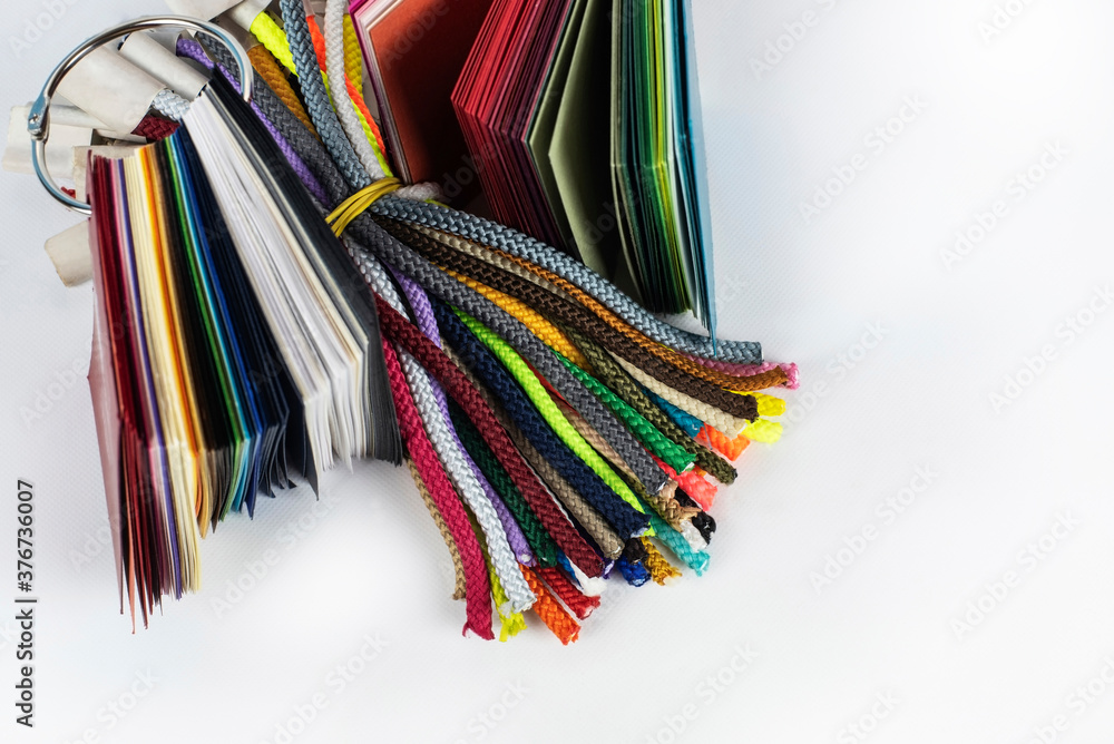 Colored laces on a light background, a catalog of different color and fabric laces for handles on paper bags next to the paper catalog of designer wrapping paper. Flat lay