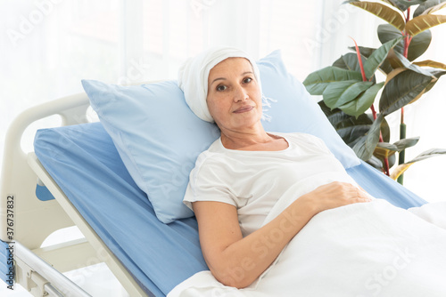 Senior breast cancer patient wearing a headscarf laying in bed and looking at the camera, cancer concept