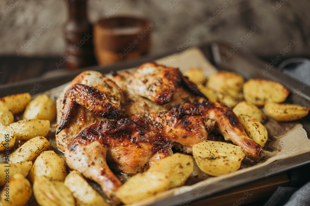 Grilled or roasted Chicken Tobacco on paper over baking sheet . Homemade freshly baked whole juicy chicken with potatoes, herbs, pepper. Selective focus, close up view. Organic country food. Grilled or roasted Chicken Tobacco on paper over baking sheet . Homemade freshly baked whole juicy chicken with potatoes, herbs, pepper. Selective focus, close up view. Organic country food.