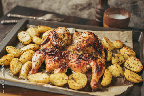 Grilled or roasted Chicken Tobacco on paper over baking sheet . Homemade freshly baked whole juicy chicken with potatoes, herbs, pepper. Selective focus, close up view. Organic country food.