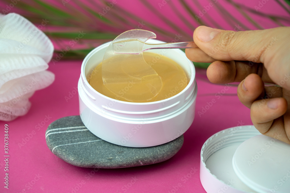 golden under eyes patches in a white container, anti aging skin care, female body care background, pink backdrop golden under eyes patches in a white container, anti aging skin care, female body care background, pink backdrop