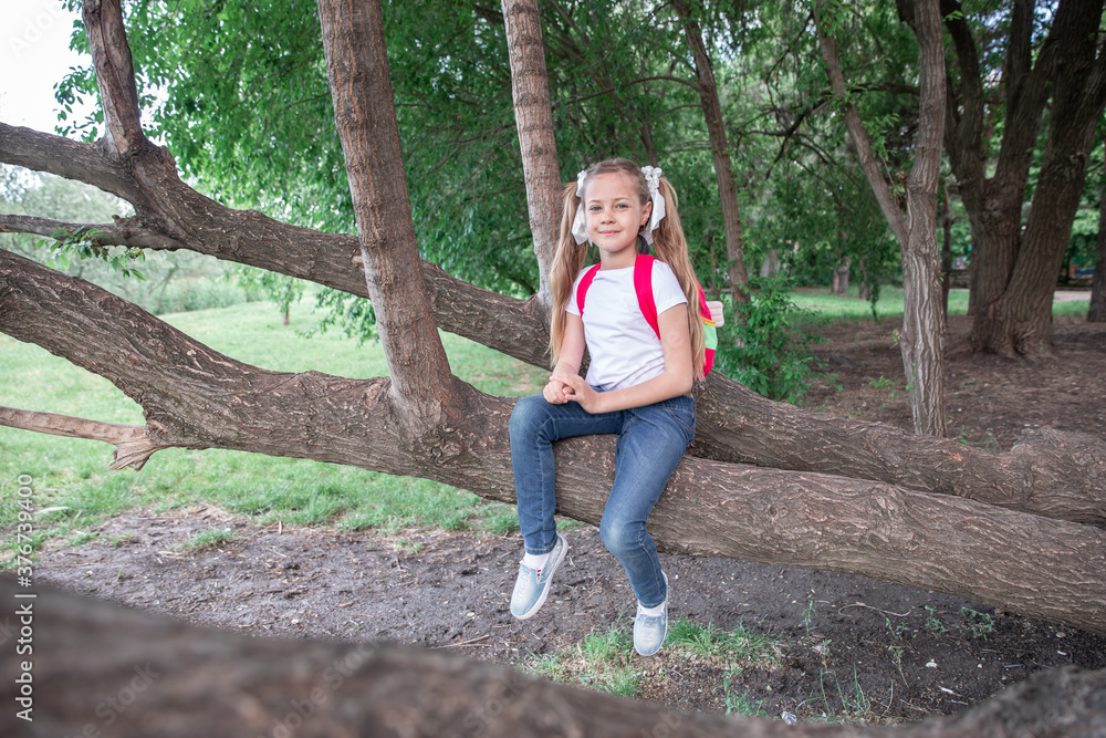 Naklejka premium a little girl sits on a tree in the woods, in the park. child and tree