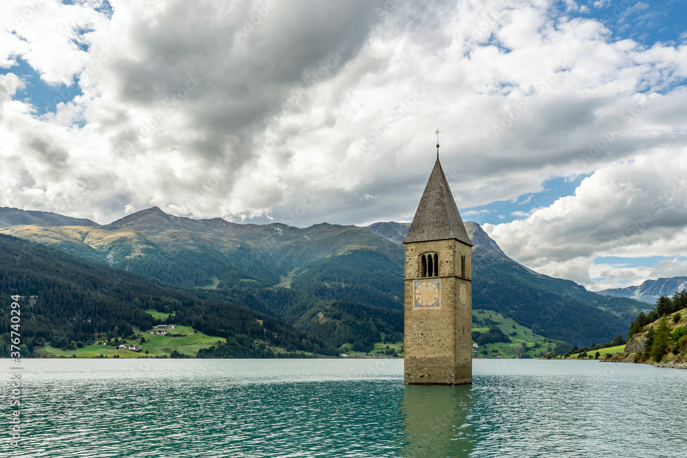 The top of the old bell tower of Curon (Graun) emerges from the waters of Lake Resia, against a dramatic sky, South Tyrol, Italy