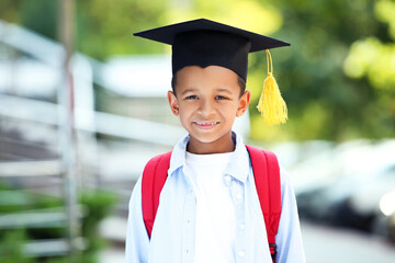 Young African American school boy with backpack and graduation cap on the street