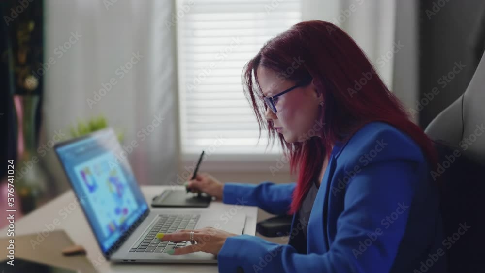 Attractive woman with glasses using a laptop and a pen. Red hair business woman working on a laptop Attractive woman with glasses using a laptop and a pen. Red hair business woman working on a laptop