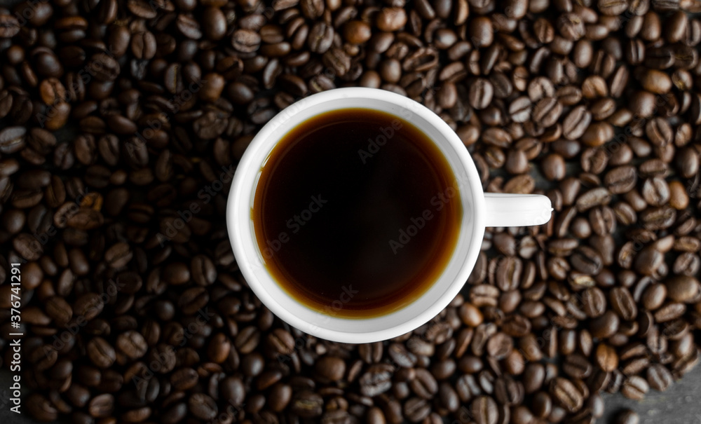White cup of coffee with roasted coffee beans background. Mug of black coffee. White cup of coffee with roasted coffee beans background. Mug of black coffee.
