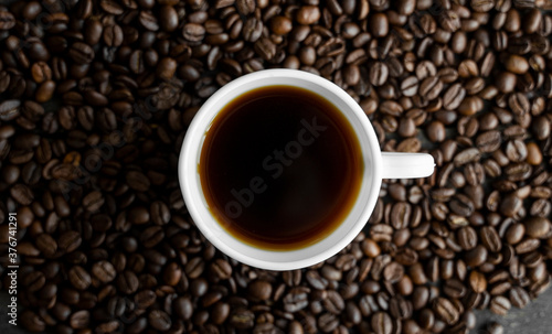 White cup of coffee with roasted coffee beans background. Mug of black coffee.