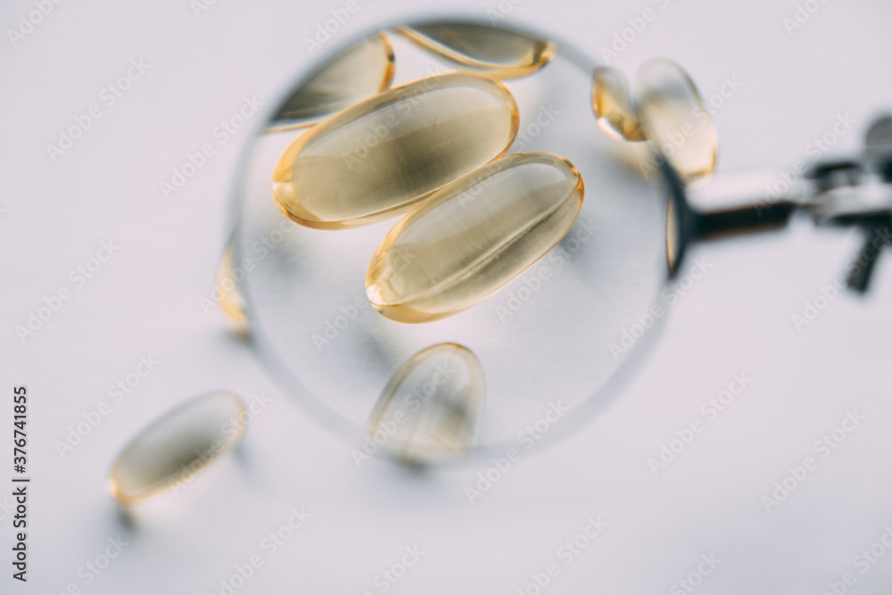 yellow transparent omega 3 capsules under a magnifying glass. vitamin development concept yellow transparent omega 3 capsules under a magnifying glass. vitamin development concept