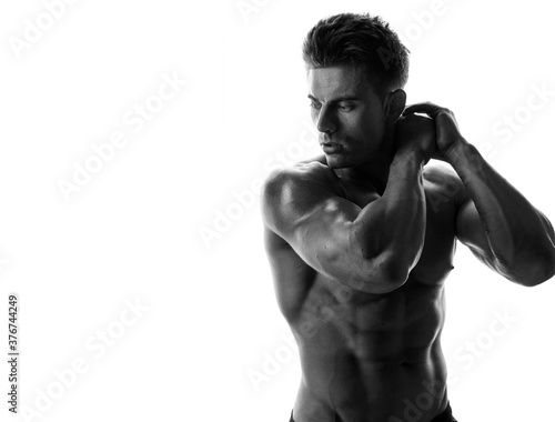 Muscular model sports young man on white background. Black and white fashion portrait of strong brutal guy. Sexy torso. Male flexing his muscles.