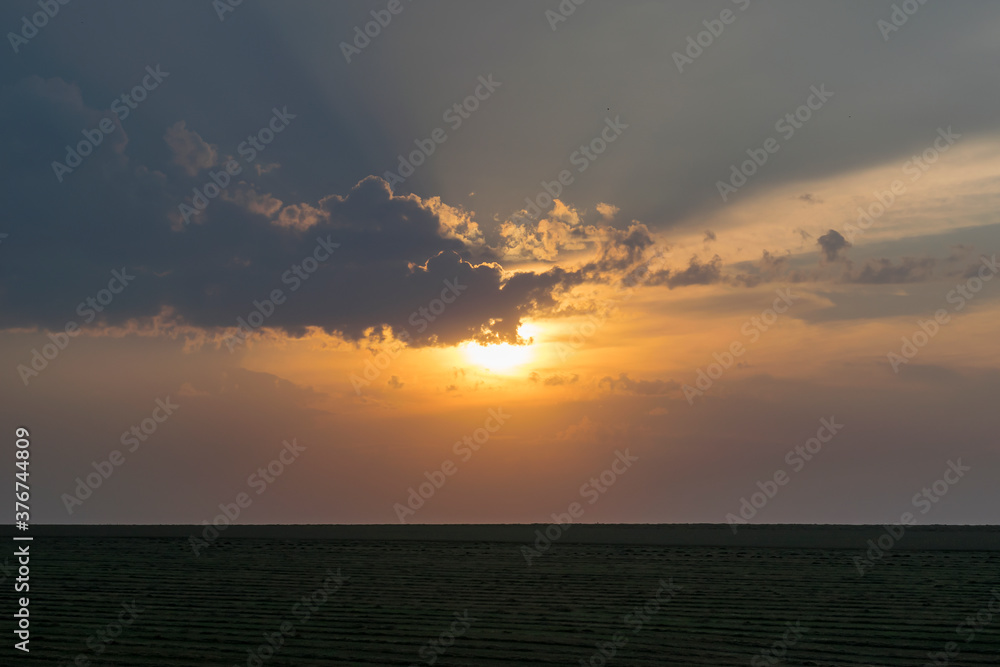 Bright sunset in cloudy weather over the field.
