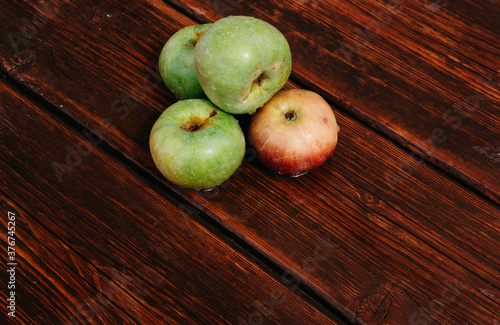 Fresh autumn Apple harvest on the kitchen countertop. Four fresh apples lie on a wooden table. A textured mahogany wood background and fruit lie on it.