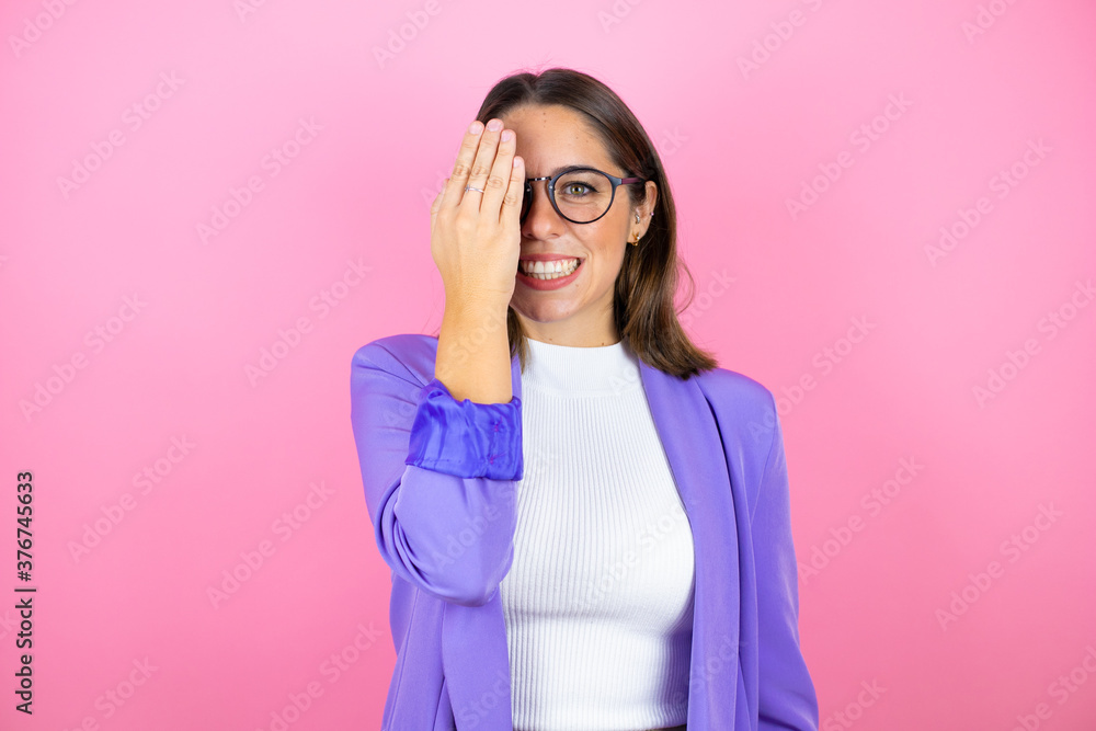 Young beautiful business woman over isolated pink background covering one eye with hand, confident smile on face and surprise emotion. Young beautiful business woman over isolated pink background covering one eye with hand, confident smile on face and surprise emotion.