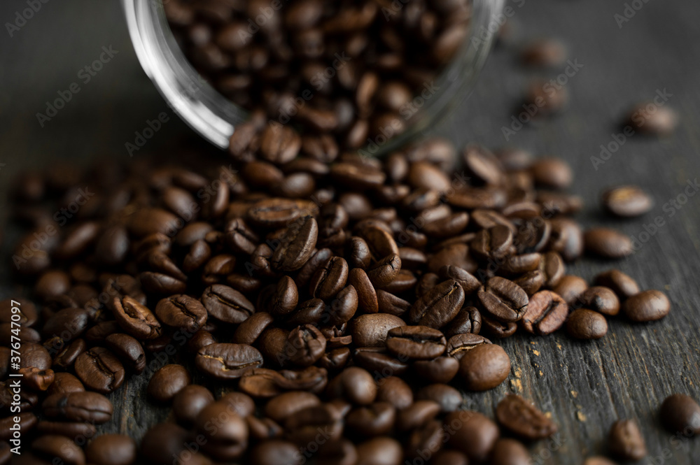 Fototapeta premium Roasted fresh arabica coffee beans scattered on a table from a little jar on a wooden table. Fresh coffee beans.