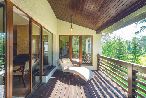Luxury private house near green forest. Soft cozy lounge chair on wooden terrace.