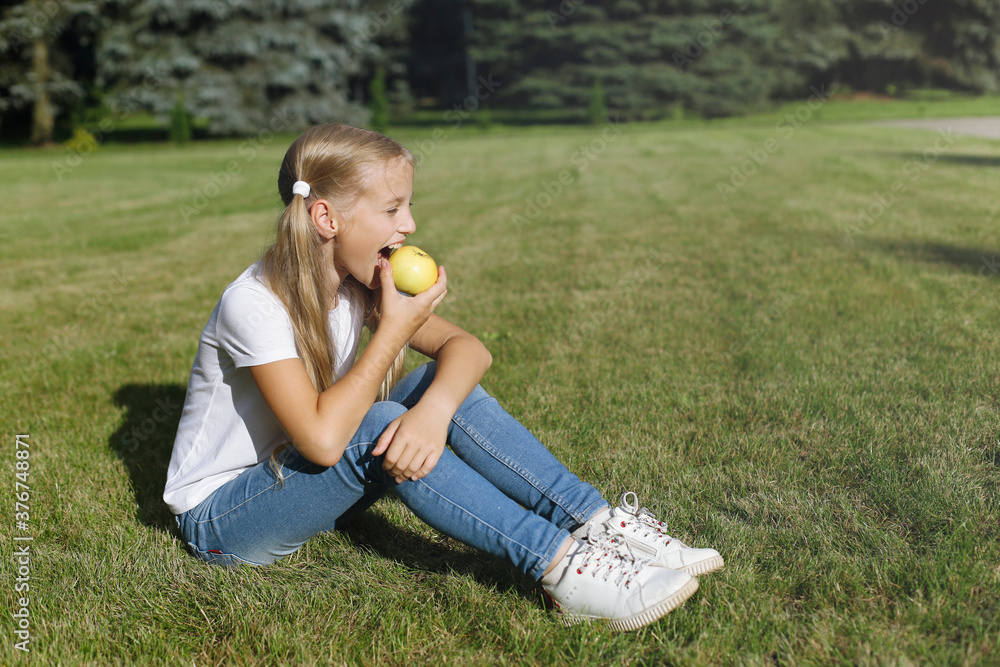 Fair-haired European girl child sitting on a green lawn and eating an apple.
Fair-haired European girl child sitting on a green lawn and eating an apple.