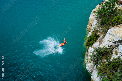Junger Mann spring von einer Klippe ins blaue Meer
