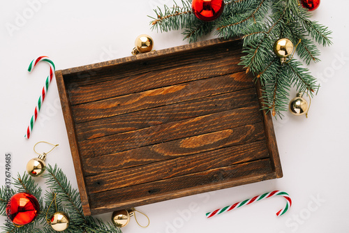 Christmas frame. Christmas balloons, garlands, red and gold ornaments, Christmas candles and fir branches with a brown wooden tray on a white background. Flatlay top view, copy space