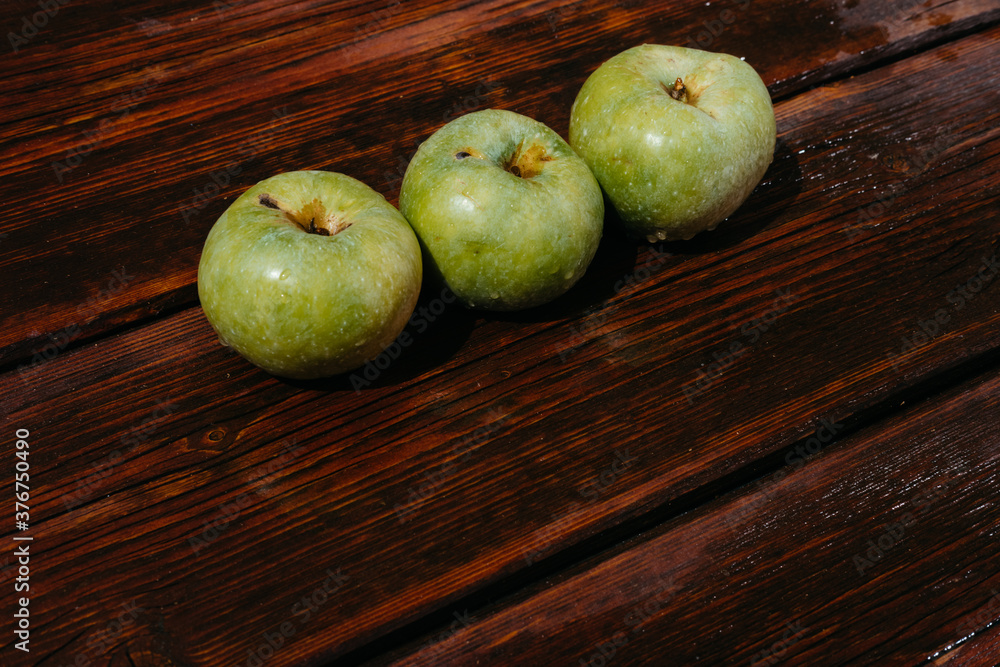 Fresh autumn Apple harvest on the kitchen countertop. Three fresh green apples lie in a row on a wooden table. A textured mahogany wood background and fruit lie on it. Fresh autumn Apple harvest on the kitchen countertop. Three fresh green apples lie in a row on a wooden table. A textured mahogany wood background and fruit lie on it.