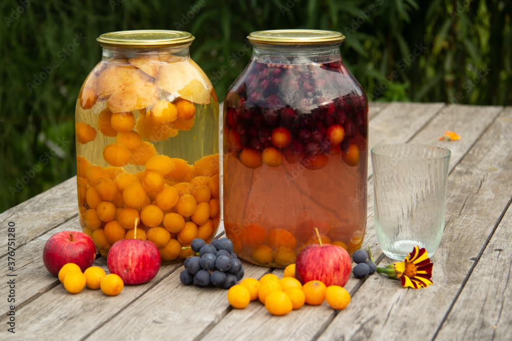 two jars of plum and grape compote stand on a wooden table on the street. home-made preparations for the winter two jars of plum and grape compote stand on a wooden table on the street. home-made preparations for the winter