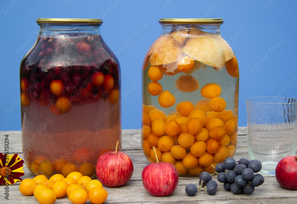Two-litre cans with compote stand on a wooden surface. There's a blue wall in the back. Homemade harvests from plums, apples, grapes Two-litre cans with compote stand on a wooden surface. There's a blue wall in the back. Homemade harvests from plums, apples, grapes