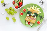 Fun food for kids - cute smiling monster face sandwich with ham and cheese, served with fresh tomatoes and cucumbers
